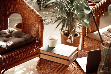 Warm and soft apartment in daytime and coffee cup with book on table around bamboo chairs and plants.