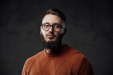 Fototapeta premium Portrait of a bearded and stylish guy with glasses he looks at camera with serious face and posing in dark background.