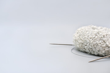 grey knitting yarn in a skein with needles on grey background. monochrome trendy image. relaxing hobby and leisure for everybody. wool yarn for winter handmade clothes.