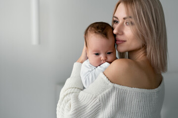 Mom is standing, holding and hugging her newborn baby. Her lips gently brush against his cheek.