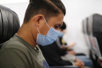 Thai man wearing the medical mask for prevent virus inside airplane during flight. Daily life after covid-19. New normal lifestyle, coronavirus and personal protection concept. selected focus.