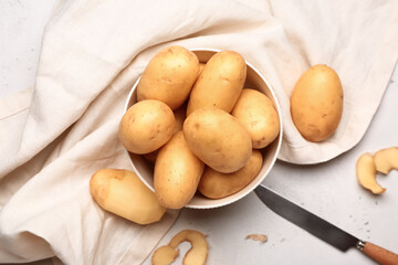 Bowl with raw potatoes on light background