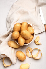 Bowl with raw potatoes on light background