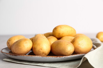 Plate with raw potatoes on light background