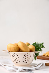 Colander with raw potatoes on light background