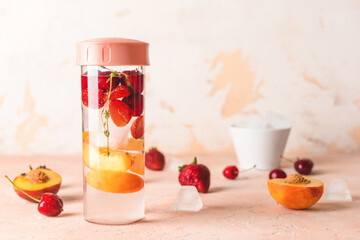 Bottle of fresh infused water with berries and apricot on light table
