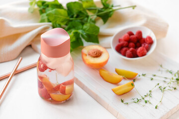 Bottle of mint infused water with raspberry and apricot on light table