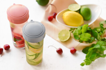 Bottles of mint infused water with berries and citrus on light table