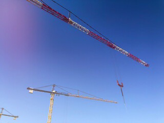 Booms of tower cranes against blue sky. Lifting machinery at construction site