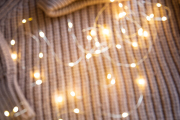 Fototapeta premium Lights of a luminous garland on a knitted sweater on the table. Background with soft focus. Christmas concept.