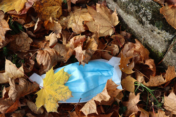 Waste during Covid-19. Medical protective face mask covered by autumn leaves in the park