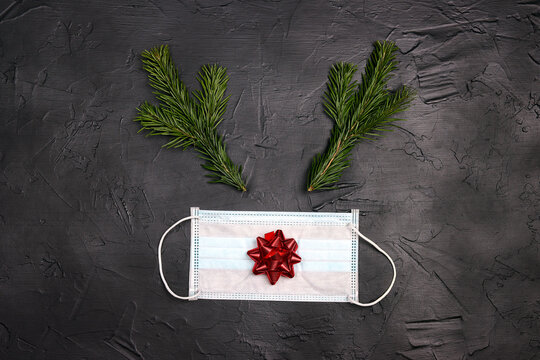 Christmas deer face made of fir-tree branches and red bow with medical mask on black background. - Powered by Adobe