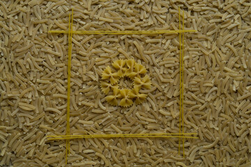 A circle of farfalle in a square of spaghetti lie on a background of noodles scattered on the table