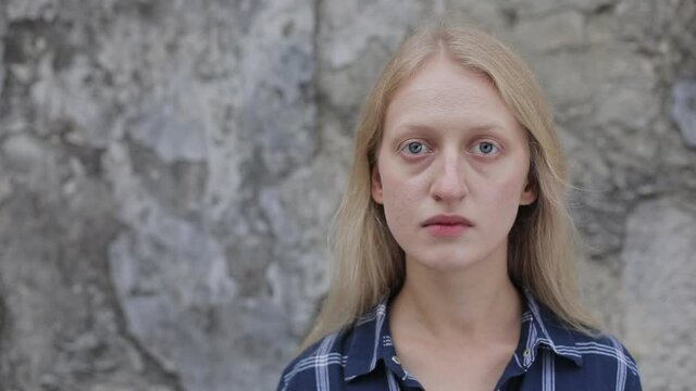 Portrait of young woman wearing shirt taking off eyes and looking to camera. Close up view of sad female person with blond hair standing at city street. Concept of headshot. Outdoors.