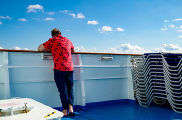 Man with bright shirt and anchors watches seascape and ocean towards horizon on cruiseship or...