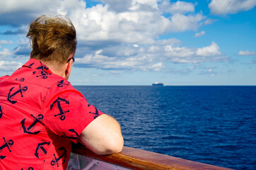Man with bright shirt and anchors watches seascape and ocean towards horizon on cruiseship or...