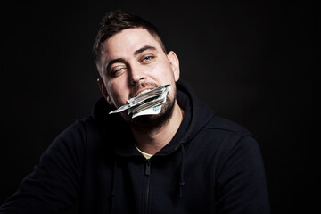 A young man holds money in his mouth. Black background. Close-up.