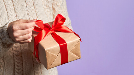 Girl holding a Christmas or New Year gift box with a red ribbon on a purple background