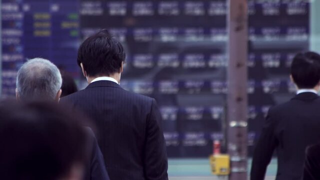 マスクをして出勤する日本人ビジネスマンと株価ボード電光掲示板