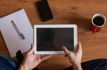 Tablet PC with black screen in the hands, cup of tea, phone and notebook on the floor. Top view