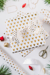 Gift boxes in white paper with golden hearts on white background. Christmas and New Year background. Gift wrap supplies.