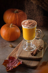Pumpkin spice latte in a glass and flying cinnamon powder in the background light. Autumn still life.