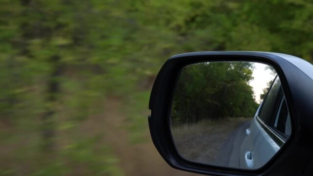 4K video of driving car on forest road, closeup front mirror view reflaction