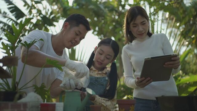 Asian couple with daughter gardening while watching laptop together 
