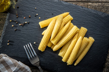 Pickled young baby corn cobs on black stone cutting board.