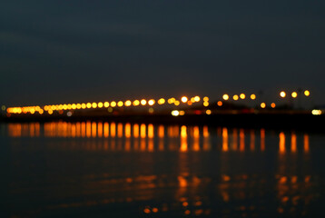 Abstract Blurred Sea Bridge at Night with the Reflections of Lighting on the Sea