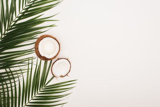 Top view of coconut halves near palm leaves on white background with copy space, stock image