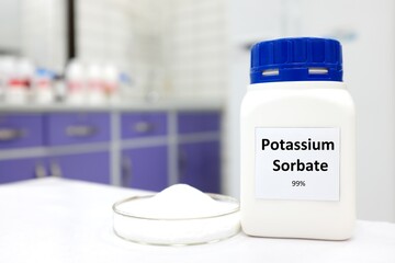 Selective focus of bottle of pure potassium sorbate food additive beside a petri dish with white solid powder substance. White laboratory background with copy space.