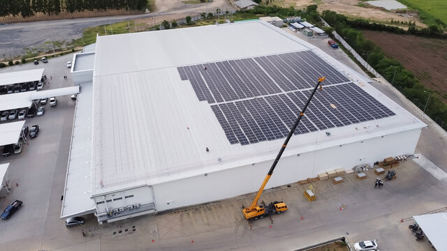 Solar panels installed on a roof of a large industrial building or a warehouse. Industrial buildings in the background. Horizontal photo.