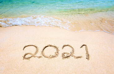 Happy New Year 2021, lettering on the beach with wave and clear blue sea. Numbers 2021 year on the sea shore, message handwritten in the golden sand on beautiful beach background. New Years concept.