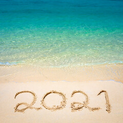 Fototapeta na wymiar Happy New Year 2021, lettering on the beach with wave and clear blue sea. Numbers 2021 year on the sea shore, message handwritten in the golden sand on beautiful beach background. New Years concept.