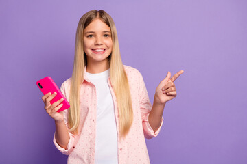 Photo of optimistic long hairdo pretty girl hold telephone point empty space wear pink shirt isolated on violet color background