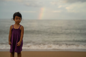 little girl standing at seashore against rainbow. 