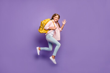 Fototapeta na wymiar Full size profile photo of optimistic pretty girl jump wave hand wear pink shirt jeans sneakers rucksack isolated on violet background