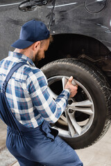 Obraz na płótnie Canvas back of repairman in workwear fixing wheel on car