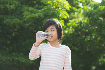 Cute asian boy drinks water from a bottle outdoors