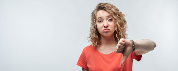 Pretty blonde girl showing thumb down. Dislike, failure gestures concept. Studio shot, white background. Copy space