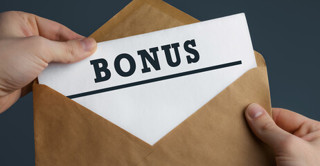 Male hands holding craft envelope with word BONUS on blue background