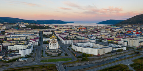 Fototapeta premium Beautiful panorama of the city of Magadan. Morning aerial view of the cathedral, streets, buildings, mountains and sea bay. A large port city in the Russian Far East. Magadan, Magadan Region, Siberia.