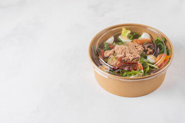 Fish diet salad with tuna, tomatoes, arugula on light background top view. Healthy vegetarian lunch.Copy space for text. Take away, food delivery in disposable plate of brown craft paper.