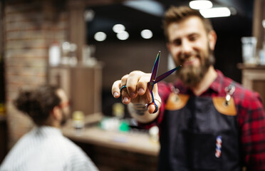 Portrait of happy young barber with client at barbershop and smiling.