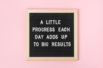 A little progress each day adds up to big results. Motivational quote on black letter board on pink...