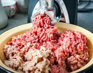 Minced meat coming out of the meat grinder on a yellow plate closeup