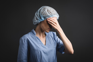  nurse in medical cap covering eyes isolated on dark grey