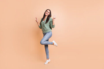 Fototapeta na wymiar Full length photo of charming joyful woman show two v-signs hello stand one leg isolated on beige color background