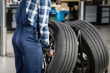 partial view of mechanic in overalls taking car wheel in workshop, stock image